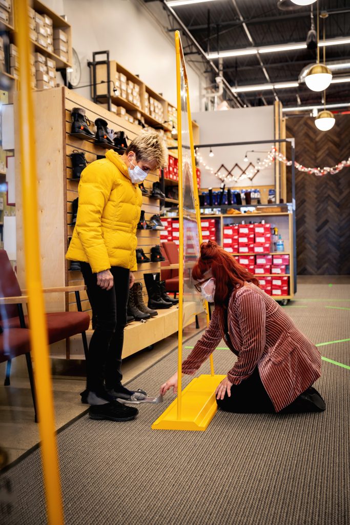 Nancy Cooper of Chelsea, gets help finding some boots from 10-year employee Carly LaForest at Mast Shoe Store in Ann Arbor. The store uses many safety protocols including screens, masks, sanitizing and marked off social distancing areas.